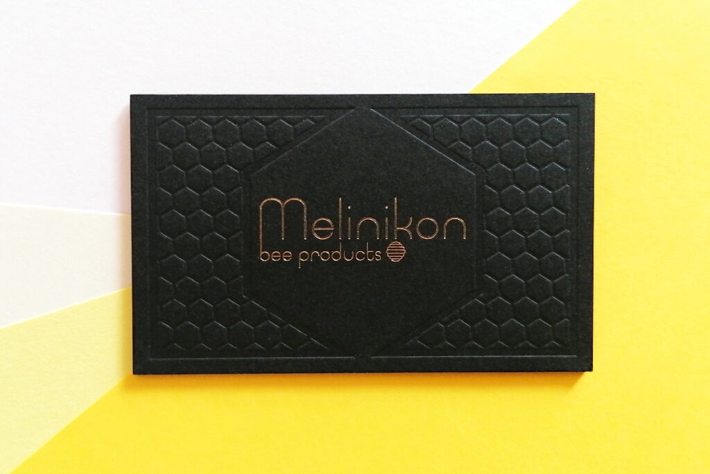 Front view of the Melinikon black board card with gold foil and blind honeycomb pattern